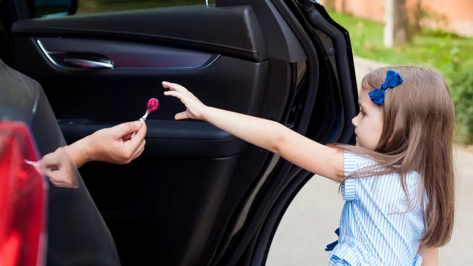 A child reaches into a strangers car. The stranger is holding out candy.
